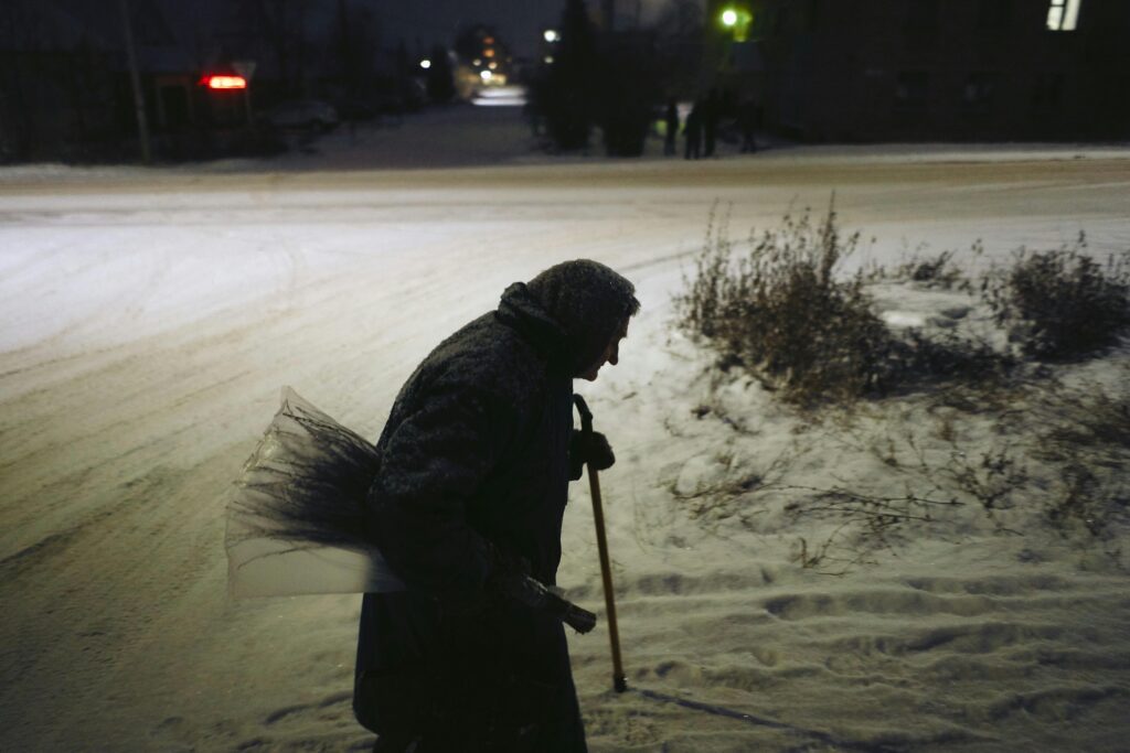 Senior woman with a cane walking during a snowy night in an urban area, side profile silhouette.