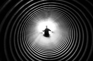 A person silhouetted against light at the end of a spiral tunnel, creating a striking black and white contrast.