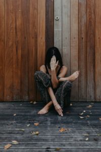 Barefoot woman with headache sitting with embracing legs and touching head in wooden floor in autumn