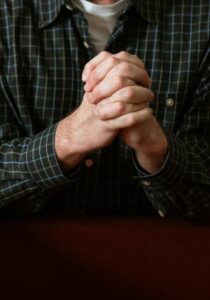 Adult man kneeling in church pew, praying with devotion in a quiet, sacred setting.